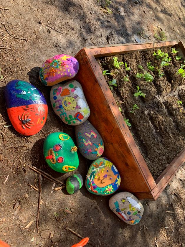Piedras pintadas por niños y niñas, al lado de un mini huerto