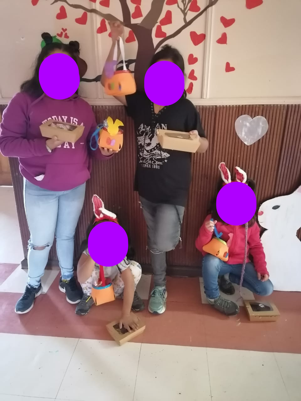 Niñas posando con los huevos de chocolate en un arbor hecho por cartulina