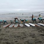 Niños en la playa, estando en la arena, pre-calentando para una clase de surf